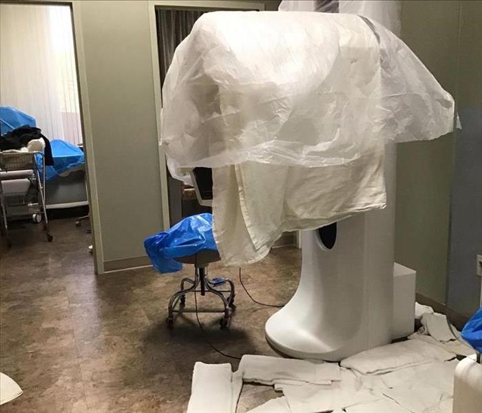 Covered medical equipment sits in a wet office with towels covering the floor.
