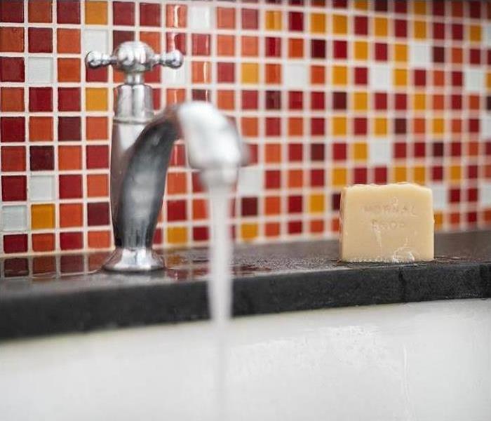 Water runs from a sink faucet in front of a colorful backsplash.